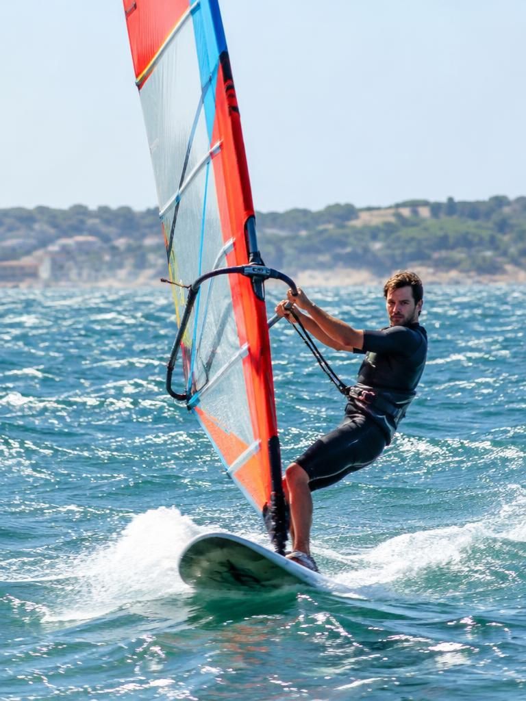 A man windsurfing across bright, choppy water.